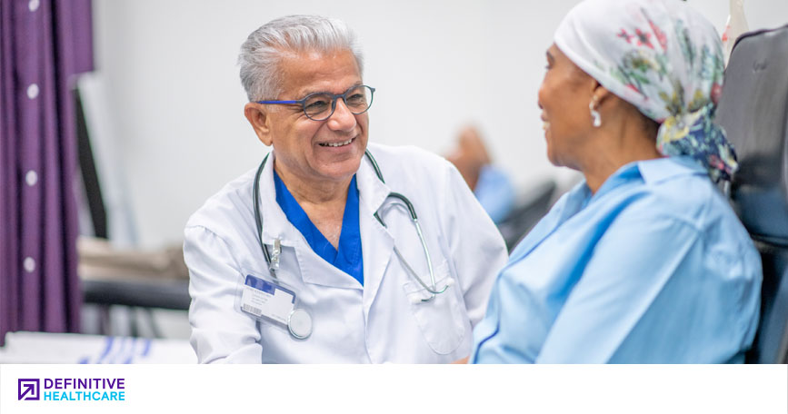 healthcare professional smiles while touching the hand of a patient who is sitting down