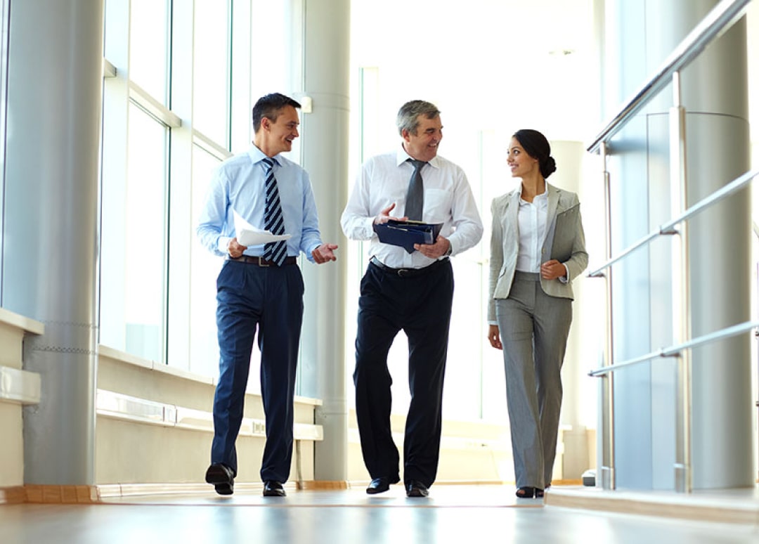 Three healthcare professionals in business attire smiling while walking with clipboards and papers in their hands.