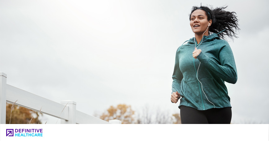 A woman goes on a run while wearing a teal hoodie. The sky behind her is overcast.