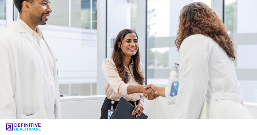 A sales professional shakes hands with a physician while another medical professional looks on.