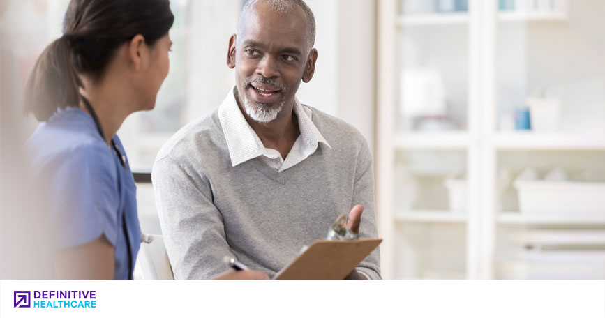 A female healthcare professional talks to a male patient in a well-lit doctor's office.